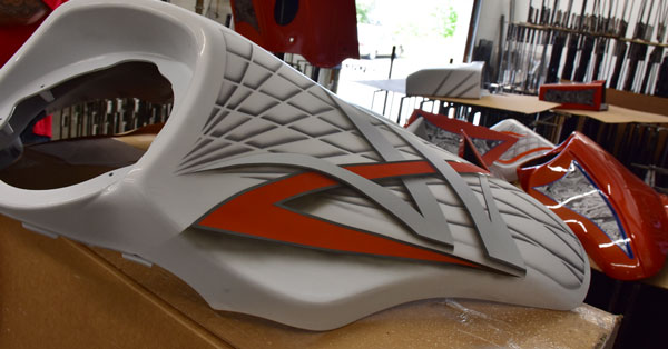 picture of a white and orange motorcycle part that was water transfer printed on, splashed hydrographics water transfer printing job on some motor cycle parts with weapon racks in the background, hydro dipping motorcycle parts white and orange