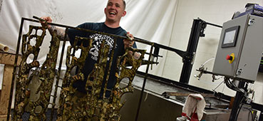 picture of a splashed hydrographics professional holding up some camouflage weapons after they were hydro dipped with a camouflage design